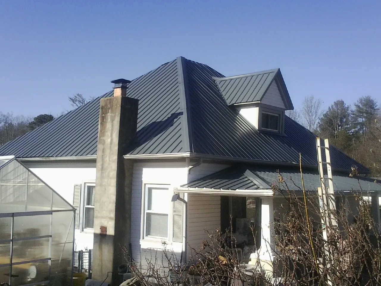 Dark blue standing seam metal roof on a white farmhouse with dormer — Slate & Tile Roof Repair by Roofing Brothers in Oak Hall