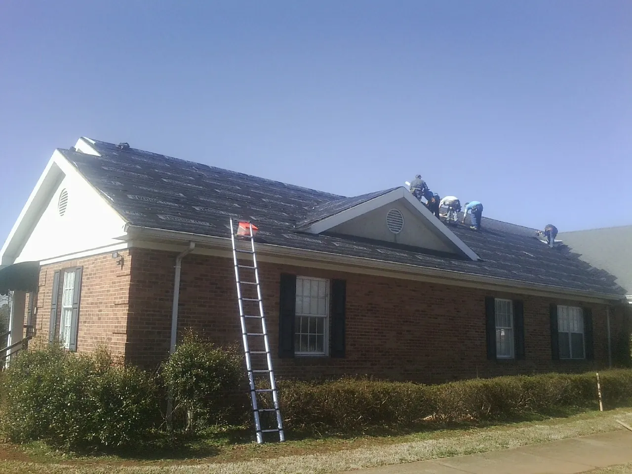 Crew tearing shingles off a brick ranch roof with a ladder set — Emergency Roof Repair work by our crew in Oak Hall