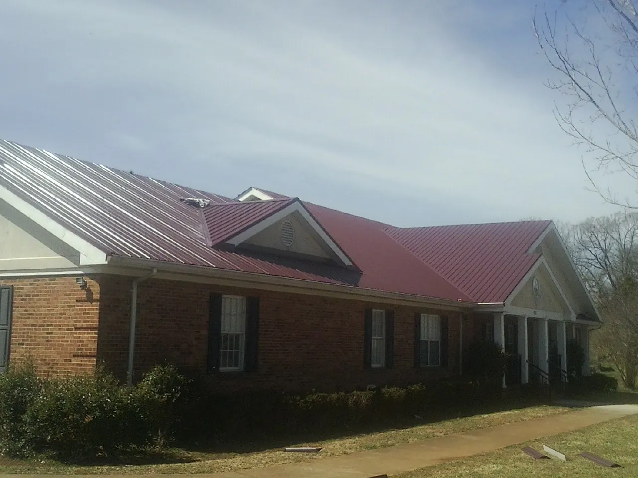 Red metal roof with gabled entries on a long brick building, from a Hail Damage Roof Repair job in Oak Hall