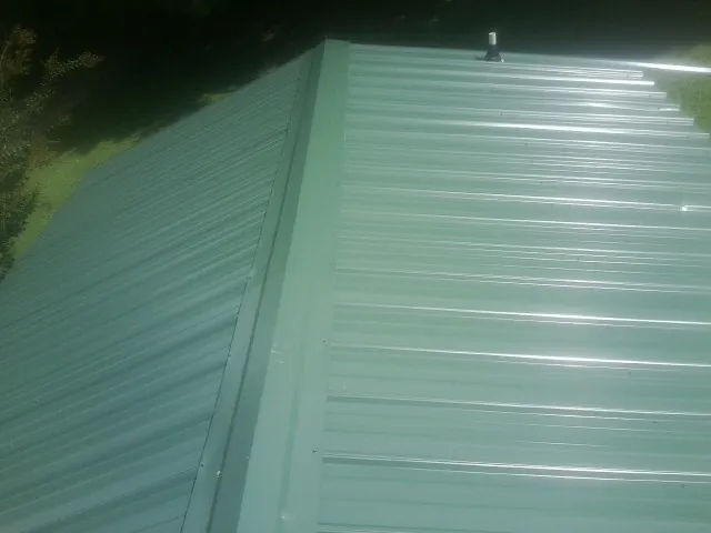 New green metal panels meeting at the ridge of a roof — Flat Roof Repair work by our crew in Oak Hall