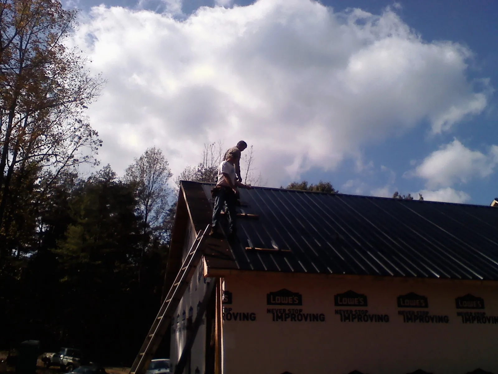Roofer fastening dark metal panels high against a cloudy sky, from a Roof Inspection job in Oak Hall