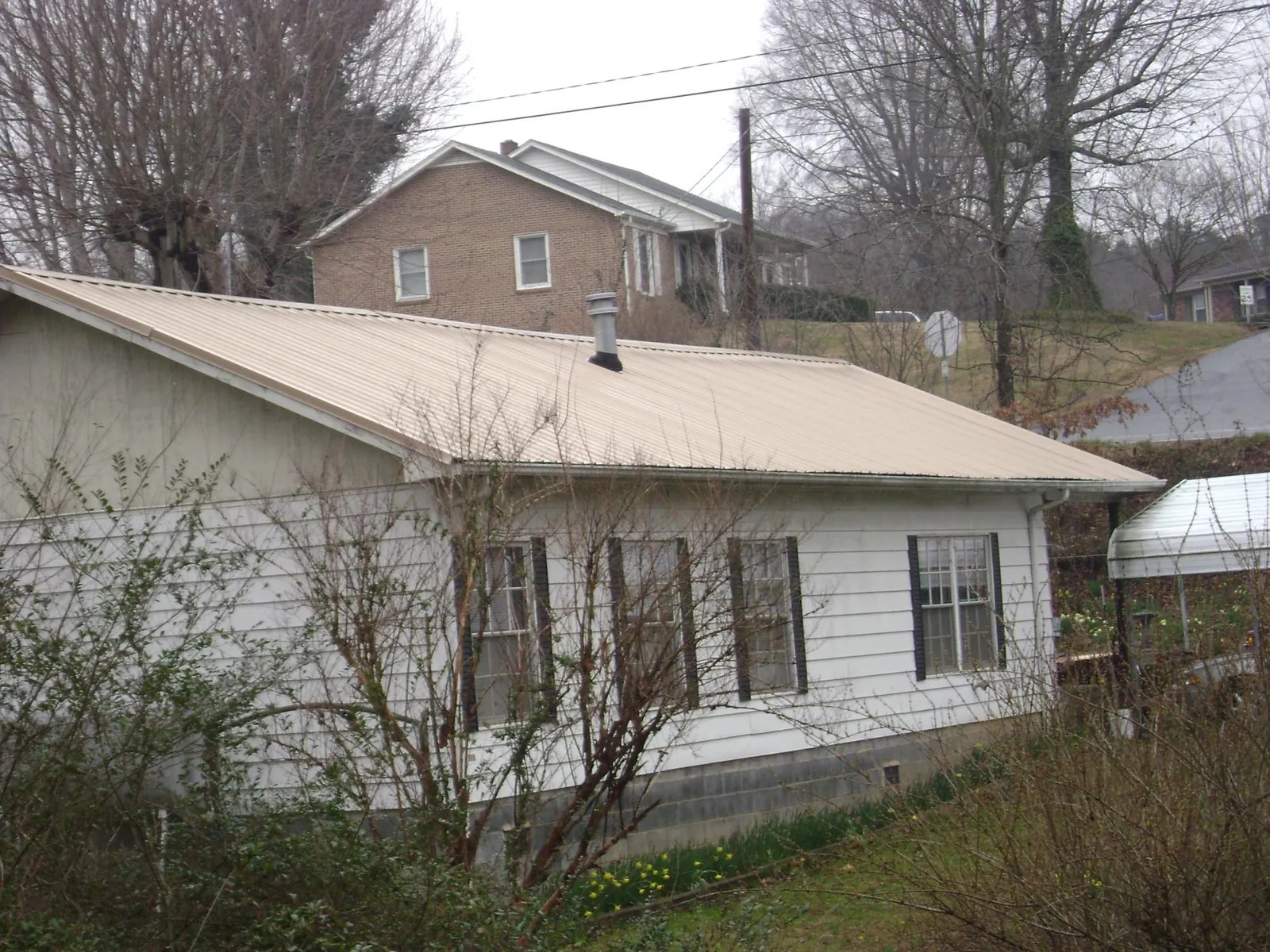 Tan metal roof on a white sided house set into a hillside — Commercial Roofing by Roofing Brothers in Oak Hall
