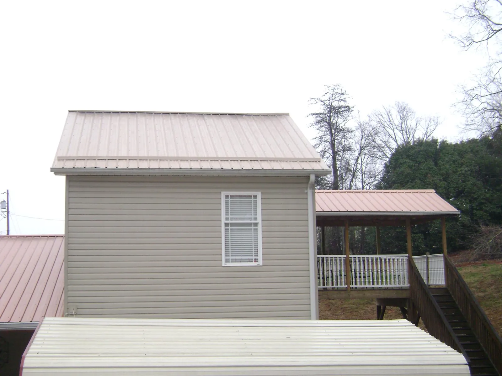 Tan metal roofs on a two story addition and attached porch, from a Roof Replacement job in Oak Hall